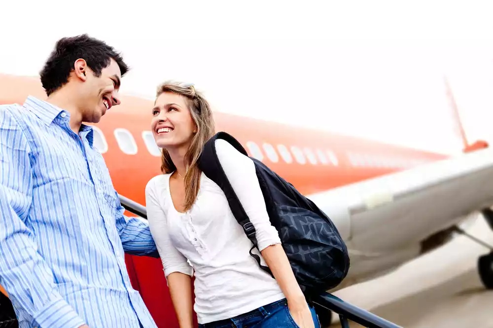 Smiling couple of travelers standing by an airplane