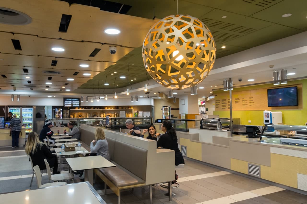 Workplace cafeteria with people eating at tables near the serving counter